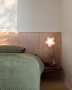 a bed with a green bedspread sitting next to a wooden headboard and night stand