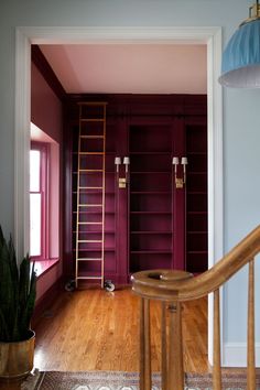 an empty room with purple painted walls and wooden shelves in the corner, next to a ladder