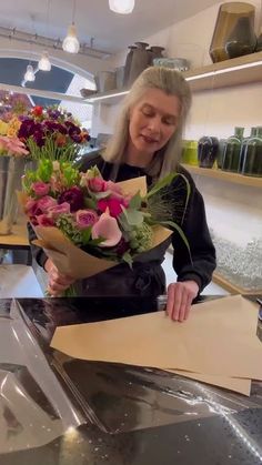 a woman standing behind a counter holding a bouquet of flowers