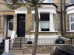 a brick house with white windows and black iron fence around the front door, on a residential street in london