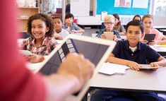 a group of children sitting at a table with an electronic device in front of them