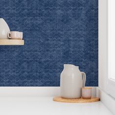 two white vases are sitting on a shelf in front of a blue striped wall