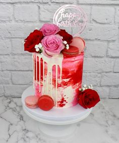 a pink and red cake with roses on top is sitting on a white pedestal in front of a brick wall