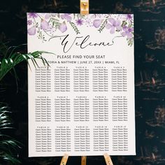 a seating sign with purple flowers and greenery sits on top of a wooden easel