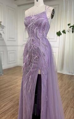 This enchanting gown in a delicate lavender hue exudes elegance and sophistication. It features intricate bead and feather embellishments, adding texture and a touch of whimsy. The gown is backless, offering a bold and alluring look. A side drape creates a soft, flowing effect that enhances the overall silhouette. This stunning piece is perfect for a glamorous evening event or a special occasion where you want to leave a lasting impression. Production time is between approx 6-8 weeks. * Sizing - Purple Sequined Gown For Debutante Ball, Elegant Lavender Tulle Evening Dress, Purple Embellished Gown For Debutante Ball, Elegant Lavender Evening Dress For Debutante Ball, Purple Embellished Tulle Gown, Glamorous Embellished Purple Gown, Glamorous Purple Embellished Gown, Draped Gown, Drape Gowns