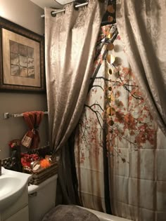 a bathroom with a shower curtain that has an autumn tree design on it, along with a white toilet and sink