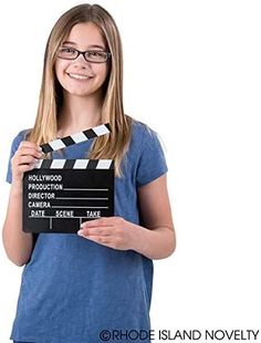 a girl holding a clapper in front of her face and smiling at the camera