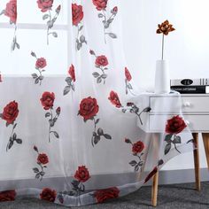 a curtain with red roses on it in front of a white dresser and window sill