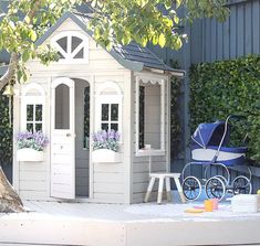 a small wooden doll house with a baby carriage in the yard next to a tree