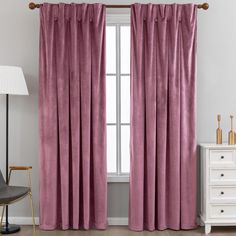 a pink curtain hanging in front of a window with a white chair and lamp next to it