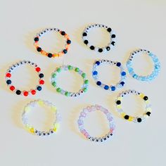 six bracelets with different colored beads are arranged on a white surface and one is in the middle