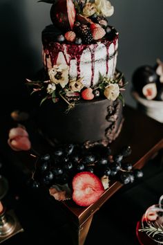 a three tiered cake with berries and flowers on top is surrounded by other desserts