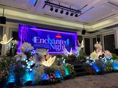 an illuminated stage with flowers and butterflies in the foreground is lit up by blue lights