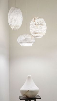 three white vases sitting on top of a black table in front of a wall