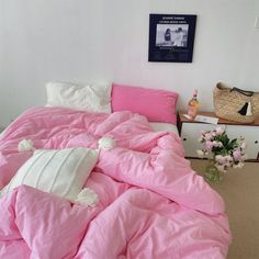 a bed with pink sheets and pillows in a room next to a basket full of flowers