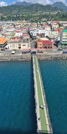 people are walking across a bridge over the water in front of some buildings and mountains