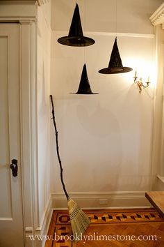 three witches hats hanging from the ceiling above a broom in front of a white wall