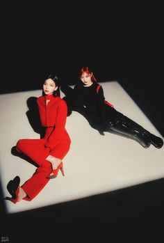 two women in red and black sitting on a white surface with their feet up to the floor