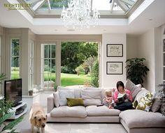 a woman sitting on top of a white couch next to a dog in a living room