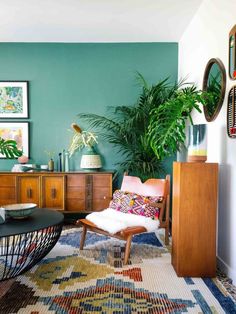 a living room filled with furniture and plants on top of a wooden dresser next to a green wall