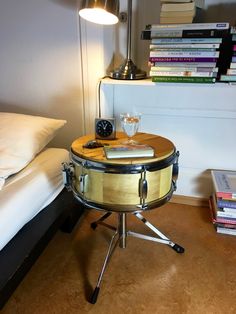 a drum sits on a table in front of a bed with books and a lamp