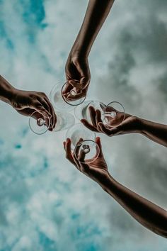 four hands holding wine glasses in the middle of a circle on a cloudy sky background