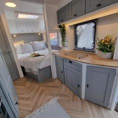 the interior of an rv with wood flooring and gray cupboards, including a bed