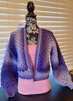 a purple crocheted jacket sitting on top of a table next to a window