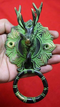 a hand holding a green and black ring with a deer's head on it