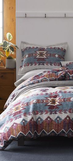 a bed with a colorful comforter on top of it next to a wooden dresser