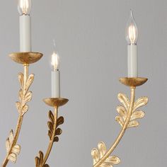 three candles that are sitting next to each other with gold leaves on the candle holders