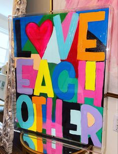 an art piece with the words love each other painted in multi - colored letters on it