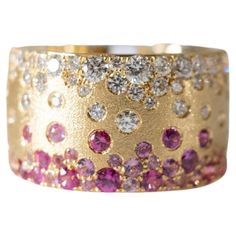 This extraordinary statement piece showcases a striking 12.3mm wide band, meticulously crafted from the finest 18 karat yellow gold. The band's luxurious satin texture adds an air of sophistication, perfectly complementing the dazzling array of gemstones that adorn it. A breathtaking collection of pink sapphires, rubies, and diamonds, totaling 0.95 and 0.77 carats respectively, are scattered and flush-set into the band, creating an eye-catching display of vibrant color and brilliance. The pink sapphires exude a soft, romantic glow, while the rubies radiate a fiery passion. The diamonds, renowned for their exceptional sparkle, add a touch of timeless elegance to the piece. Ring size: 6.5 This ring is available in custom sizes. Please contact us with your preferred size for a price quote and Wide Band Diamond Ring With Pave Setting, Yellow Gold Wide Band Ring With Single Cut Diamonds, Luxury Wide Band Diamond Ring, Luxury Wide Band Diamond Cut Ring, Yellow Gold Wide Band Ring With Brilliant Cut, Luxury Wide Band Yellow Gold Ring, Confetti Ring, Pink Sapphire Band, Sapphire Eternity Band