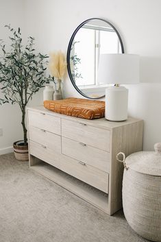 a white dresser with a mirror and vase on it next to a potted plant