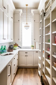 a kitchen with white cabinets and wood flooring next to an open pantry filled with food