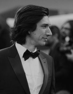 a man in a tuxedo is looking off to the side while people are taking pictures