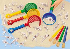 a child's hand is holding a plastic scooper and spoons on the sand