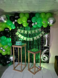 balloons and streamers are set up on the wall behind two stools in front of a green backdrop