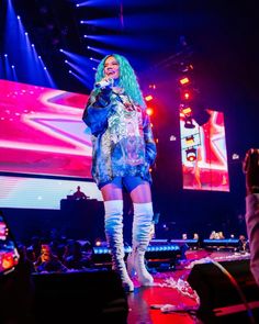 a woman standing on top of a stage holding a microphone in her hand and wearing thigh high boots