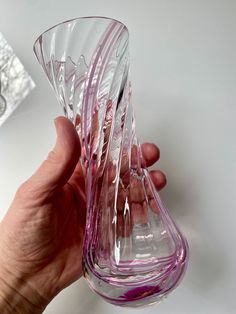 a hand holding a pink glass vase on top of a table