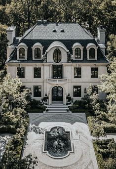 an aerial view of a large white house surrounded by trees and bushes with a fountain in the front yard