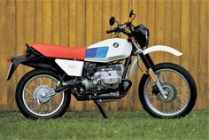 black and white photograph of a motorcycle parked in front of a wooden fence on grass