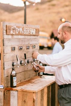 a man standing next to a wooden table filled with beer bottles and tappers on top of it