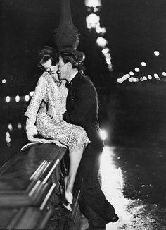 an old photo of a man and woman kissing in front of a river at night