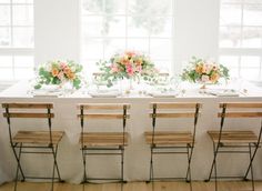 the table is set with four chairs and flowers on it, along with place settings