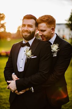 two men in tuxedos embracing each other on the grass at sunset or dawn