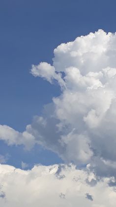 the airplane is flying high in the sky with clouds behind it and blue skies above