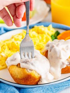 someone is holding a fork over an english muffin on a plate with scrambled eggs