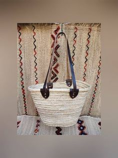 a large woven basket with leather handles hanging on a curtain in front of a window