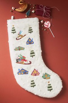 a white christmas stocking with houses and candy canes next to it on a red surface